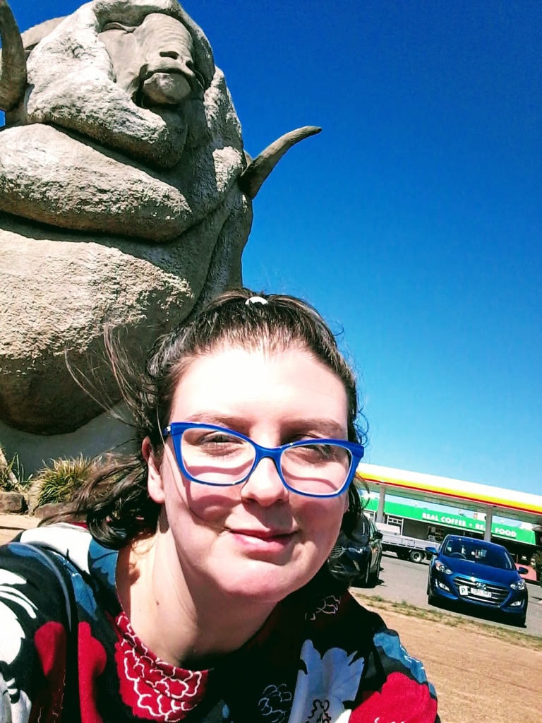 Picture of Lizzie Knight outside in Australia in front of large sculpture of a ram - the Big Merino in Goulburn, Australia (pre-COVID lockdowns)